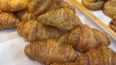 Tepside sergilenen taze kruvasanların çeşitliliği. Klasik tereyağlı kruvasan, çikolata dolu kruvasan, bademli kruvasan ve lezzetli seçenekler içeriyor. Altın, yumuşak hamur işleri kahvaltı için mükemmeldir.