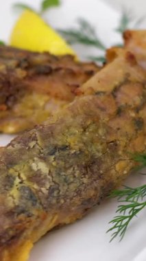 Kızarmış kuyruk bölümü ve kırsal masada beyaz bir tabakta limon dilimleriyle süslenmiş diğer sazan dilimleri, rotasyon sırasında üst görünüm. Yüksek kalite 4k görüntü
