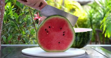 Altın saat boyunca açık havada canlı yeşil kabuklu sulu kırmızı karpuzu dilimleyen taze, olgun karpuz, yumuşak doğal parçalarla çevrili tabakta kesiliyor..