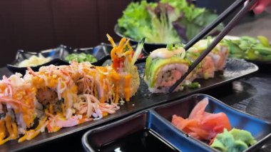 Geleneksel Japon mutfağının en iyi manzarası. Somon, ton balığı ve sebzeli suşi ruloları siyah taş masada servis edilir. Siyah taş üzerinde yemek çubuklarıyla Asya yemeği. Kamera hareketi. Yüksek