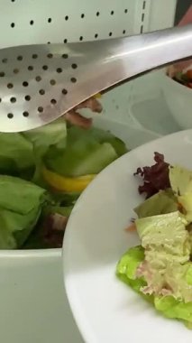 Fresh salad with lettuce leaves and tomato falling into bowl, served with healthy food ingredients on white table, slow motion. High quality 4k footage