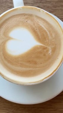 Latte lezzetli aromatik kahve kapuçino masanın üzerinde duruyor ve kamera da fincan sanatının kalbinin etrafında dönüyor. Yüksek kalite 4k görüntü