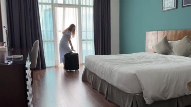Otel Odasına varış: Bir otel odasında bavulunu boşaltmaya hazır genç bir kadın duruyor, manzara sakin ve dinlenme ve seyahat izlenimi uyandırıyor. Yüksek kalite 4k görüntü