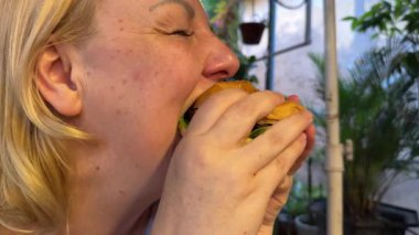 Kafkas kadın müşteri müşterisi abur cubur yiyor hamburger çiğniyor, hamburger çiğniyor, zevk alıyor beslenme düzenini aldatıyor, yemek cezbediyor. Sağlıksız abur cubur, aşırı kalori tüketimi..