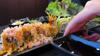 Sushi siyah tabakta yuvarlanıyor, yakın plan. Japon mutfağı. Dönüyor. Soya sosu, zencefil ve güzel dekore edilmiş wasabi.