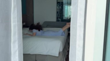 Kız yüz üstü yere düşüyor. Pencere manzaralı. Mavi elbise, yatak odası, dinlenme, dinlenme. Yüksek kalite 4k görüntü