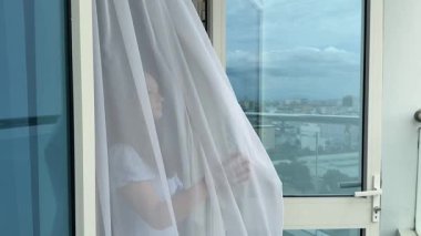 Pattaya otel odasının açık cam kapısından esen deniz esintisi ince perdeyi sallıyor. Genç kız mavi elbisesiyle balkona çıkıyor.