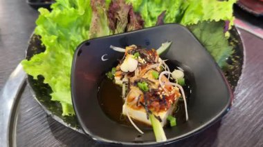 Siyah bir tabakta bir restoranda şifalı bitkilerle deniz ürünleri servis etmek muhteşemdir. Tofu salatası.