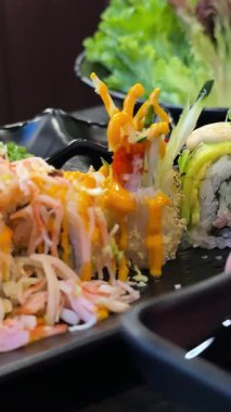 Sushi siyah tabakta yuvarlanıyor, yakın plan. Japon mutfağı. Dönüyor. Soya sosu, zencefil ve güzel dekore edilmiş wasabi.