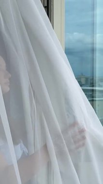 Pattaya otel odasının açık cam kapısından esen deniz esintisi ince perdeyi sallıyor. Genç kız mavi elbisesiyle balkona çıkıyor.