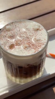 Köpüklü buzlu latte ve kafedeki bardağa koyu kahve dökülüyor.