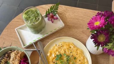 Sağlıklı tropik meyve suyu kutusu ahşap bir masada duruyor. Kahvaltı muz, müsli, meyve ve yeşillik, omlet ve kibrit çiçekleriyle dengelenir. Yüksek kalite 4k görüntü