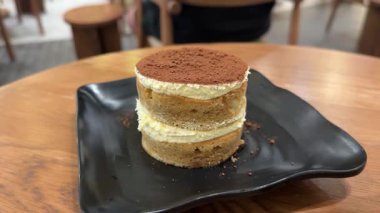 Bir kafede bir parça tiramisu kırmanın tadını çıkarın. Siyah yuvarlak bir tabakta. Lezzetli bir kahve, tatlı, kalori. Yüksek kalite 4k görüntü