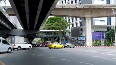 Şehir trafiği Bangkok 'taki Skytrain raylarının altından geçiyor, arabalar, otobüsler, motorsikletler yüksek gökdelenler arasında karmaşık bir kavşakta ilerliyorlar. Bangkok Tayland 06.06.2025