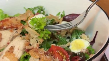 Çatalla Sezar salatası yemek. Tavuk fileto, marul, domates, bıldırcın yumurtası, kızarmış ekmek ve parmesan peynirinden yapılmış sağlıklı bir salata. Yüksek kalite 4k görüntü