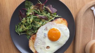 Croque Madame veya ızgara peynirli jambon ve yumurtalı ahşap kesim tahtası. Sandviç kızartılmış ve cıvık bir sarısı var. Yüksek kalite 4k görüntü
