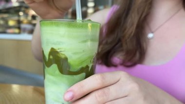 Bir kafede elinde buzlu kibritli latte tutan, pipet içeceği soğutucusuyla karıştıran bir kız. Yüksek kalite 4k görüntü