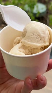 Beyaz bardakta dondurma, karamel serpiştirilmiş ve karamelli, tahta kaşıkla serpiştirilmiş. Yüksek kalite 4k görüntü