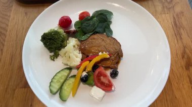 Kızarmış domates, sarımsak ve taze bitkilerle birlikte beyaz tabakta ızgara biftek ve yanında bezelye. Aşçılık sanatı ve güzel yemek sunumu. Yüksek kalite 4k görüntü