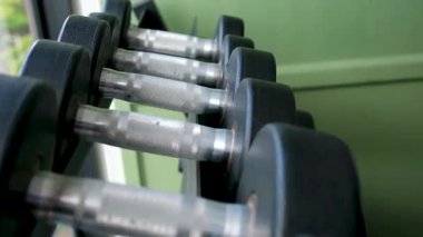 Spor salonunda ağırlık rafları ve arka planda görünen banklar gibi dayanıklılık eğitimi ekipmanlarıyla düzenli halterlerin sıra sıra odak çekimini yapın. Yüksek kalite 4k görüntü