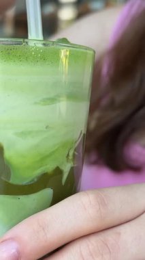 Bir kafede elinde buzlu kibritli latte tutan, pipet içeceği soğutucusuyla karıştıran bir kız. Yüksek kalite 4k görüntü