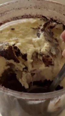 Sütlü yulaf, kahve ve çikolata parçacıkları ve kahve çekirdekleri ile kaplı şeffaf cam bir kapta nefis bir tiramisu. Ahşap bir masaya kurulmuş mavi bir clo ile