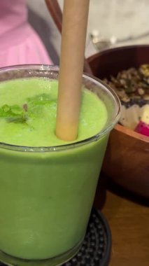 Tohumlar, fındıklar ve parçalanmış hindistan cevizi kabuğuyla servis edilmiş canlı yeşil smoothie kasesinin keyfini çıkaran bir kadının yakın plan fotoğrafı. Yüksek kalite 4k görüntü