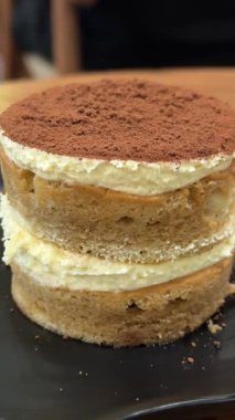 Bir kafede bir parça tiramisu kırmanın tadını çıkarın. Siyah yuvarlak bir tabakta. Lezzetli bir kahve, tatlı, kalori. Yüksek kalite 4k görüntü