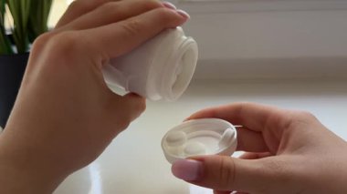 Kadın plastik kabarcıktan ya da beyaz şişe haplarından kapsül balık yağı haplarından birini alıp palmiyeye döker. Bir adet yuvarlak kalsiyum hapı. Kadınları parmaklarıyla yuvarlar. Yiyecek takviyesi vitaminleriyle oynar..