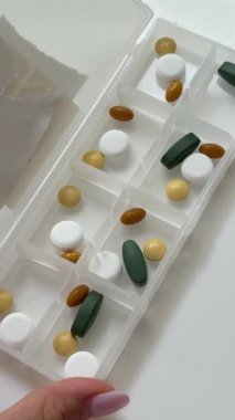 Kadın ilaç kutusunu sarı kapsüllerle dolduruyor. Beyaz masada arka planda haplar olan bir şişe. Sağlık ve tıp konsepti. Yüksek kalite 4k görüntü