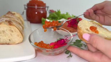 Tereyağlı ekmek ve kırmızı havyar. Kırmızı havyar, ahşap tahtada tereyağlı ekmeğin üzerine kaşıkla konuyor, açık bir havyar kutusuyla birlikte, aperatif ya da gurme için hazır. Güzel yemek. 4k