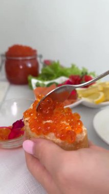 Tereyağlı ekmek ve kırmızı havyar. Kırmızı havyar, ahşap tahtada tereyağlı ekmeğin üzerine kaşıkla konuyor, açık bir havyar kutusuyla birlikte, aperatif ya da gurme için hazır. Güzel yemek. 4k