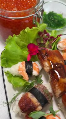 Stüdyo ışıkları altında deniz tarağı, ton balığı ve somon balığıyla birlikte saşimi suşi tabağına nazikçe sokulmuş somon yumurtası görüntüsü. Yüksek kalite 4k görüntü