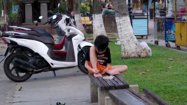 Üzgün küçük bir çocuk Asya 'da motosikletlerin arka planında bir bankta oturuyor. Hoi Bir Vietnam 10.02.2025 