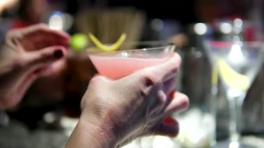 Barmen kokteyl olarak şampanya bardağına buz koyar. Eller yakın çekim. Siyah zemin üzerinde dönen kağıt uçak kokteyli