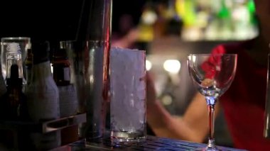 Barmen barın tezgahında kokteyl hazırlamak için şişeden cigger 'a likör dolduruyor. Arka planda hassasiyet ve canlı yeşil neon ışıklara odaklanıyor. Yüksek kalite 4k görüntü