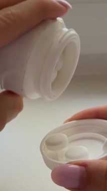 Kadın plastik kabarcıktan ya da beyaz şişe haplarından kapsül balık yağı haplarından birini alıp palmiyeye döker. Bir adet yuvarlak kalsiyum hapı. Kadınları parmaklarıyla yuvarlar. Yiyecek takviyesi vitaminleriyle oynar..