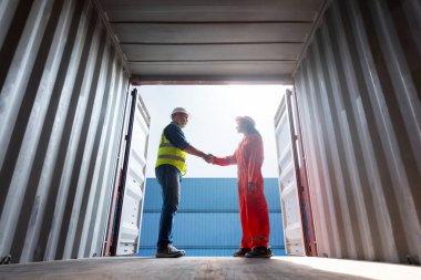 Mühendis ve işçi ekibi konteynır tersanesinde el sıkışıyor, Foreman kadını konteynır, lojistik nakliye, ihracat, başarı ve takım çalışması konseptini kontrol ediyor.