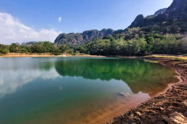 Manzara berrak su, dağlar ve ağaçlarla dolu bir göldür.