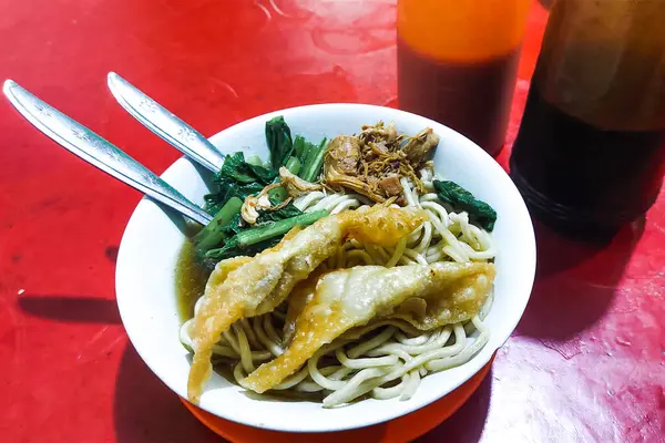 Erişteleri beyaz bir kasede, kaşıkta ve çatalda yemeye hazır.