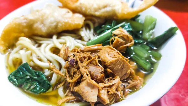 Erişteleri beyaz bir kasede, kaşıkta ve çatalda yemeye hazır.