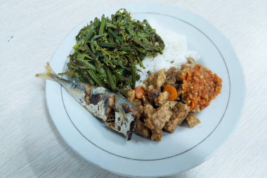 Kızarmış balık ve sebzelerle karıştırılmış pirinç beyaz bir tabakta, masanın üstünde.