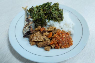 Kızarmış balık ve sebzelerle karıştırılmış pirinç beyaz bir tabakta, masanın üstünde.