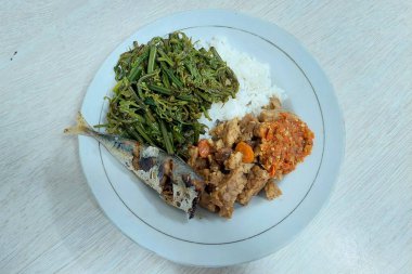 Kızarmış balık ve sebzelerle karıştırılmış pirinç beyaz bir tabakta, masanın üstünde.