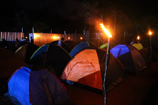 You can see a camp with conical tents lined up surrounded by torches at night