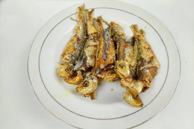 Yemek masasındaki beyaz tabakta küçük kızarmış balık.