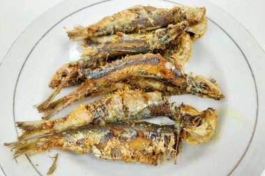 Yemek masasındaki beyaz tabakta küçük kızarmış balık.