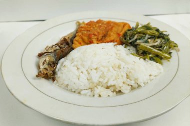 Kızarmış balık ve sebzelerle karıştırılmış pirinç beyaz bir tabakta, masanın üstünde.