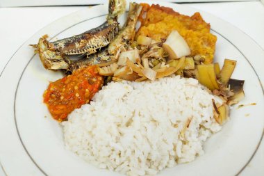 Kızarmış balık ve sebzelerle karıştırılmış pirinç beyaz bir tabakta, masanın üstünde.