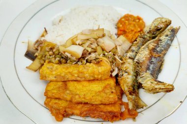 Kızarmış balık ve sebzelerle karıştırılmış pirinç beyaz bir tabakta, masanın üstünde.